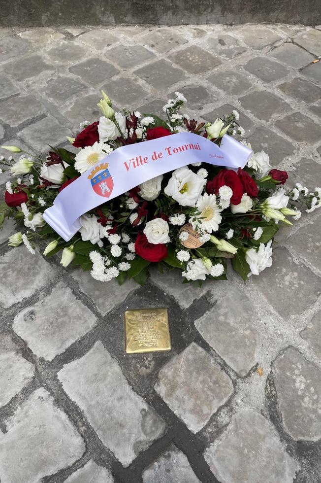 Une gerbe de fleurs avec un ruban "Ville de Tournai" posée devant la pierre d'achoppement